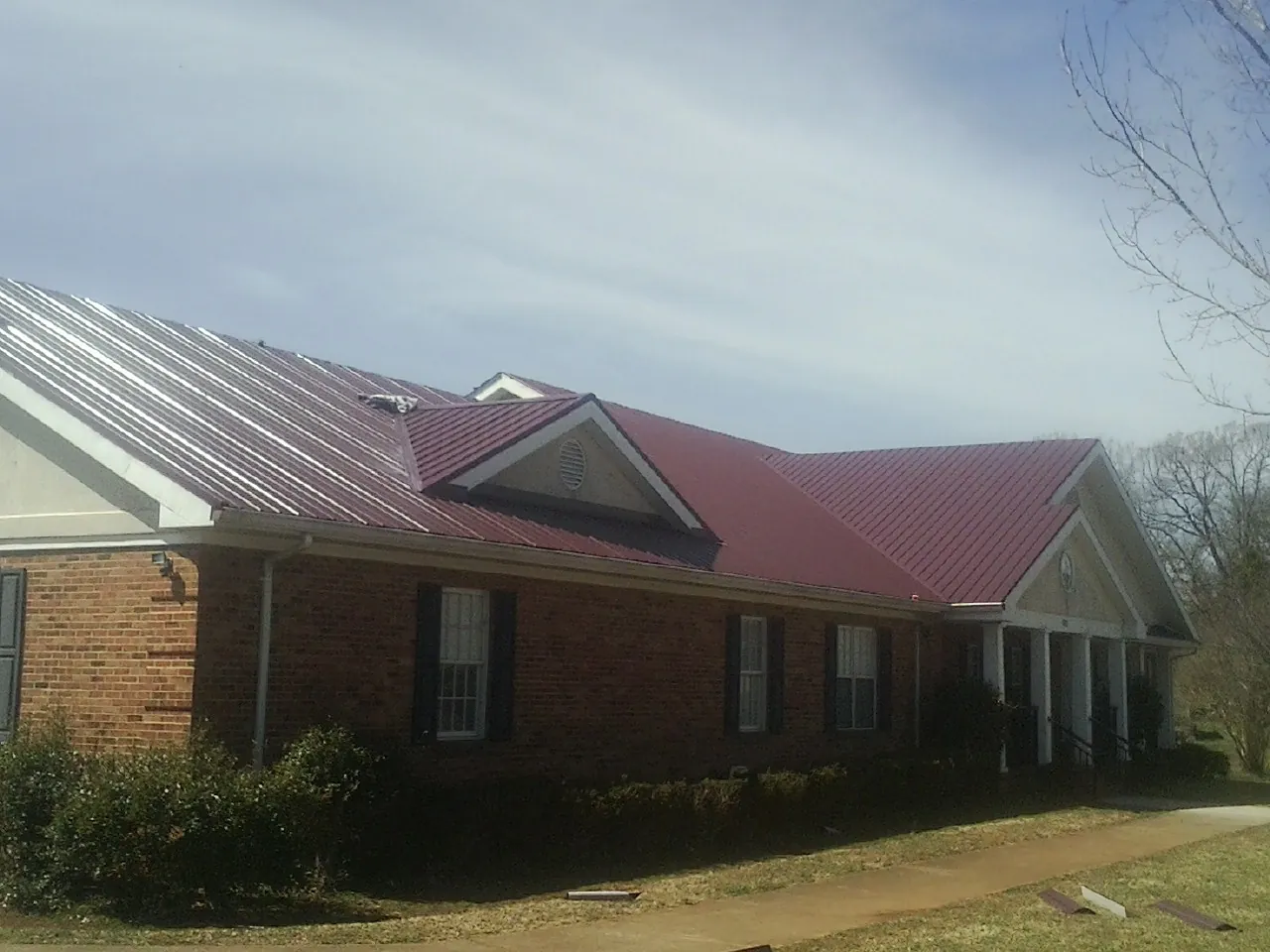 Red metal roof with gabled entries on a long brick building, from a Hail Damage Roof Repair job in Broad Top