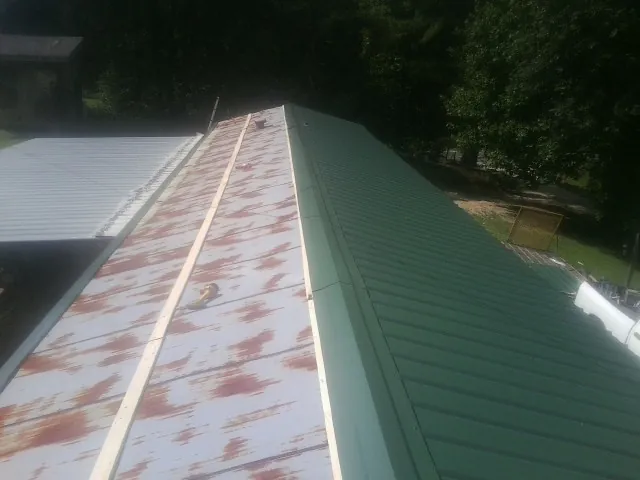 Old rusted panels beside newly installed green metal roofing — Wind Damage Roof Repair by Roofing Brothers in Broad Top