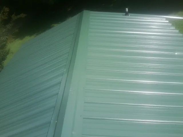 New green metal panels meeting at the ridge of a roof — Flat Roof Repair work by our crew in Broad Top