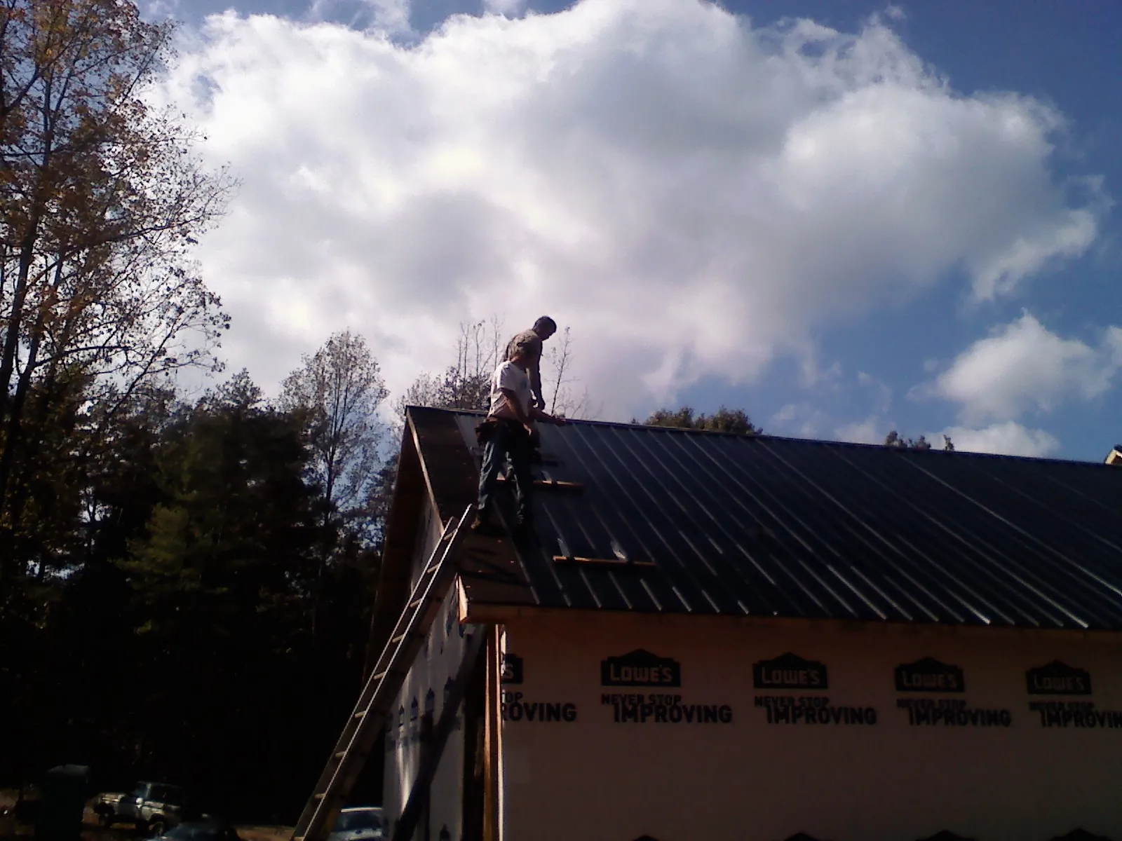 Roofer fastening dark metal panels high against a cloudy sky, from a Roof Inspection job in Broad Top