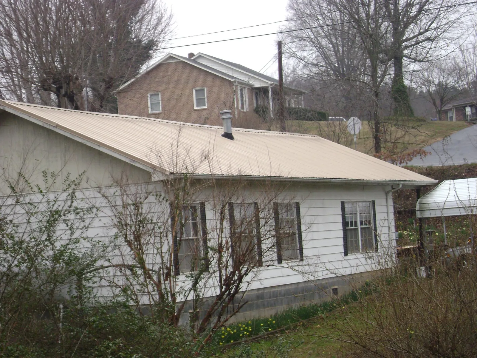 Tan metal roof on a white sided house set into a hillside — Commercial Roofing by Roofing Brothers in Broad Top