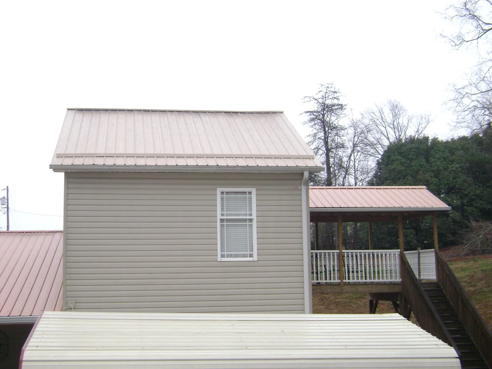 Tan metal roofs on a two story addition and attached porch, from a Roof Replacement job in Broad Top